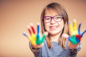 young girl with paint covered hands in braces after early orthodontics